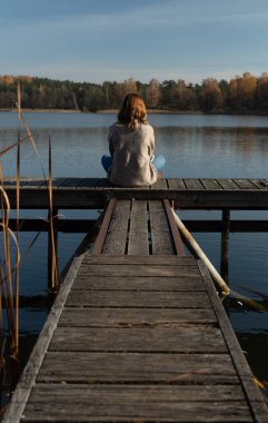 Litvanya, Trakai 'deki Galve gölüne tanıklık ederken iskelenin tepesinde oturan çekici genç bir kadın. Trakai bu Baltık Cumhuriyeti 'nin eski başkentiydi..