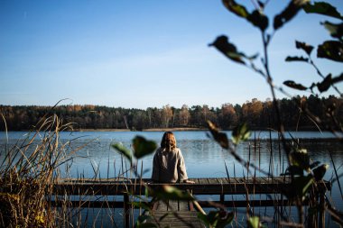Litvanya, Trakai 'deki Galve gölüne tanıklık ederken iskelenin tepesinde oturan çekici genç bir kadın. Trakai bu Baltık Cumhuriyeti 'nin eski başkentiydi..