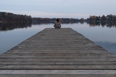 Litvanya, Trakai 'de bir gölün manzarasının tadını çıkarırken iskelenin kenarında oturan çekici genç bir kadın. Bu şehir bu Baltık Cumhuriyeti 'nin eski başkentiydi..