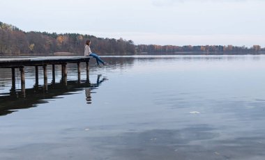 Litvanya, Trakai 'de bir gölün manzarasının tadını çıkarırken iskelenin kenarında oturan çekici genç bir kadın. Bu şehir bu Baltık Cumhuriyeti 'nin eski başkentiydi..