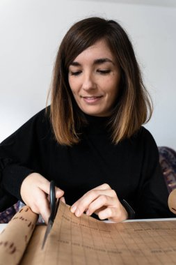 Çekici genç bir kadın Noel hediyesi olarak bir kitabı sarmak için kullanacağı geri dönüşümlü ambalaj kağıdını kesiyor.