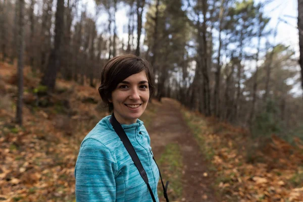 Portrait of a young sporty female hiking up from a valley to the top of a mountain while holding a camera used to take photos of the environment.