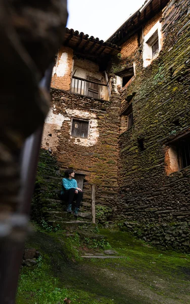 年轻迷人的女性 身穿五颜六色的夹克 坐在一座老房子的楼梯上 目睹着一座古老的小村庄的建筑 — 图库照片