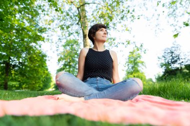 Çekici bir genç kadının portresi parkta bacak bacak üstüne atmış ve yazın Hyde Park, Londra 'da eğleniyor.