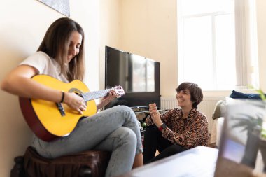 Çekici genç bayan gitarıyla şarkı söylerken arkadaşı dinleyip alkışlar ve kahkahalarla neşeleniyor.