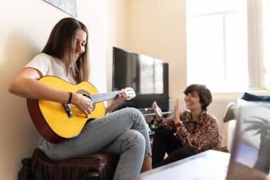 Çekici genç bayan gitarıyla şarkı söylerken arkadaşı dinleyip alkışlar ve kahkahalarla neşeleniyor.