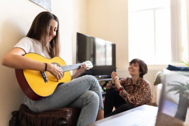 Arkadaşı onu dinlerken ve alkışlar ve kahkahalarla neşelenirken genç ve çekici bir kadının gitar çaldığı fotoğraf.