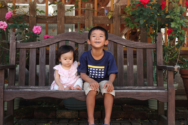 Japanese brother and sister (5 years old boy and 0 year old girl) sitting on the bench