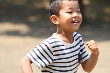 Çimenlerin üzerinde koşan Japon çocuk (ilkokulbirinci sınıf)