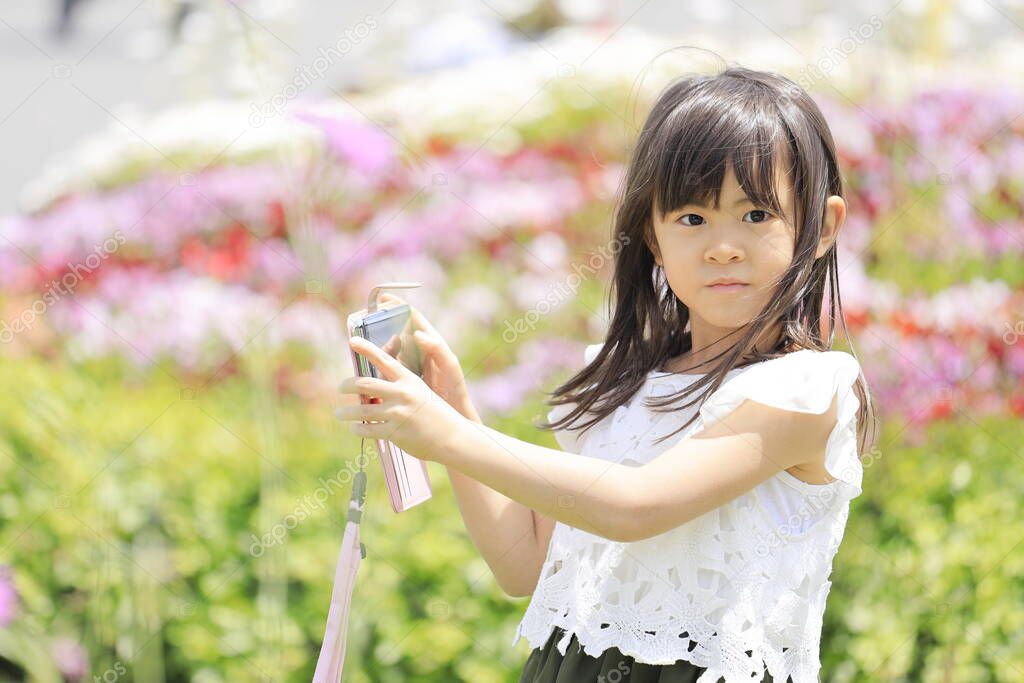 Japanese student girl taking pictures with smart phone in flower garden (6 years old)