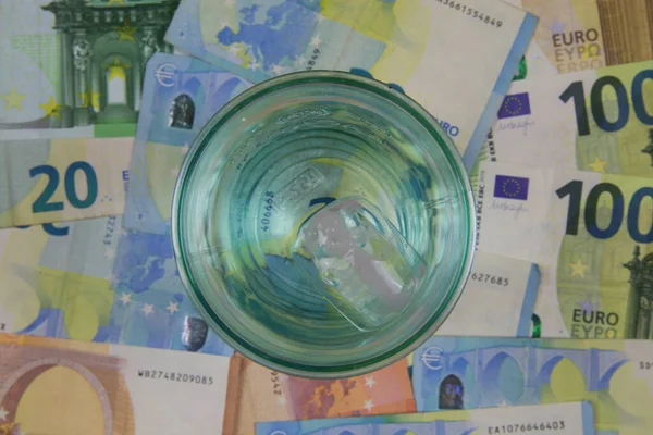 Top view on drinking glass with euro money currency banknotes background - price of affordable potable drinkable water concept