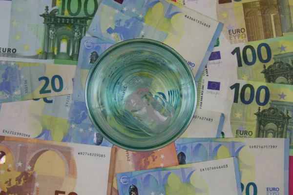 Top view on drinking glass with euro money currency banknotes background - price of affordable potable drinkable water concept