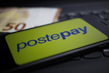Viersen, Almanya - 9 Nisan. 2020: Cep telefonu ekranının kapatılması ve bilgisayar klavyesinde Postepay ödeme sağlayıcısının logosu bulanık euro para arkaplanı
