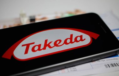 Viersen, Almanya - 9 Nisan. 2020: Cep telefonu ekranını Takeda ilaç şirketinin logosu, bulanık haplar ve laboratuvar geçmişi ile kapat