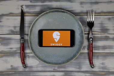 Viersen, Almanya - 9 Mayıs. 2020: Tabak ve çatal bıçakla ahşap masada sallanan yemek dağıtım servisinin logosu olan cep telefonu ekranını kapat (merkeze odaklan)