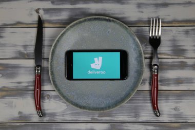 Viersen, Almanya - 9 Mayıs. 2020: Tabak ve çatal bıçaklı ahşap masaya yemek teslimatının logosu olan cep telefonu ekranını kapat (merkeze odaklan)