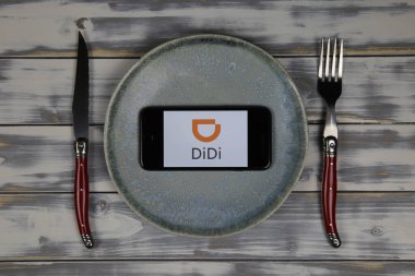 Viersen, Almanya - 9 Mayıs. 2020: Tabak ve çatal bıçak ile ahşap masada yemek dağıtım servisi didi logosu bulunan cep telefonu ekranını kapat (merkeze odaklan)