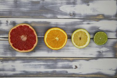 Arka arkaya dört izole edilmiş meyve parçasının yukarıdan görünüşü, kırmızı olgun greyfurt, turuncu, sarı limon ve yeşil kireç beyaz doğal ahşap masa üzerinde metin için yer var.
