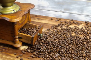 Eski, izole, ahşap ahşap kahve öğütücüsü çekmecesini kapatıyorum. Kahverengi ahşap masa üzerinde çiğ fasulye yığını var.