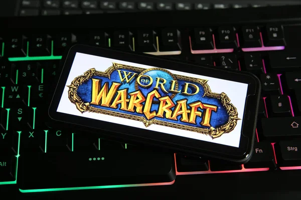 Viersen, Almanya - 9 Ocak. 2021: Akıllı telefon ekranının, aydınlatmalı bilgisayar klavyesinde online oyun dünyası Warcraft logosu ile kapatılması