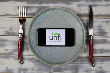Viersen, Almanya - 9 Şubat. 2021: UNFI 'nin logo harfleriyle akıllı telefon ekranının kapanışı, tabaktaki doğal gıdaları çatal bıçakla birleştirdi
