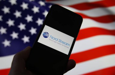 Viersen, Almanya - 9 Şubat. 2021: Nord akım doğalgaz boru hattının logosu ile telefon ekranının kapatılması, Amerikan bayrağının arka planını bulanıklaştırdı