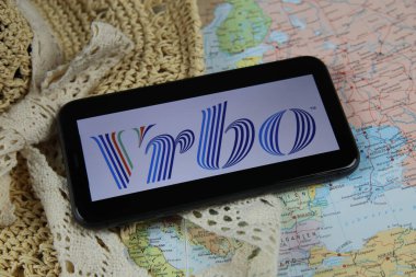 Viersen, Germany - March 1. 2021: Closeup of mobile phone screen wit logo lettering of online booking travel agency vrbo with sun hat and map clipart