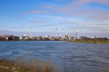Krefeld (Uerdingen) - 1 Mart. 2021: Sanayi bölgesinde mavi gökyüzüne karşı fabrikaları ve bacaları olan nehir ren manzarası