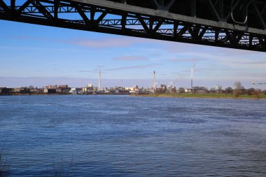 Krefeld (Uerdingen) - 1 Mart. 2021: Mavi gökyüzüne karşı fabrikaları ve bacaları olan nehir ren üzerinde çelik köprünün ötesine bakın