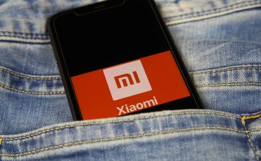 Viersen, Almanya - 1 Mart. 2021: Mavi kot pantolonlu Çinli Xiaomi cep telefonu şirketinin logo harfleriyle akıllı telefon ekranının kapatılması