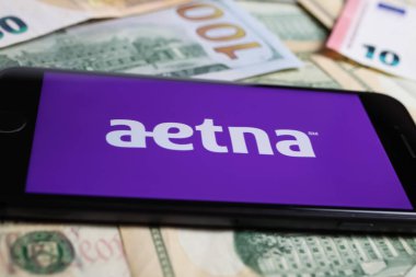 Viersen, Germany - March 1. 2021: Closeup of smartphone with logo lettering of aetna health insurance company on paper money currency clipart