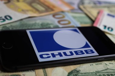 Viersen, Germany - March 1. 2021: Closeup of smartphone with logo lettering of chubb insurance company on paper money currency