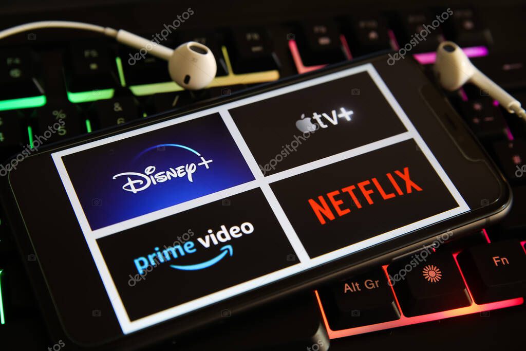Viersen, Germany - March 1. 2021: Closeup of mobile phone screen with logo lettering of various tv movie streaming services on laptop keyboard