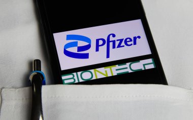 Viersen, Almanya - 9 Mayıs. 2021: Beyaz doktor ceketinin cebinde Pfizer ve Biontech eczacılık şirketlerinin logo harfleriyle cep telefonu ekranının kapatılması