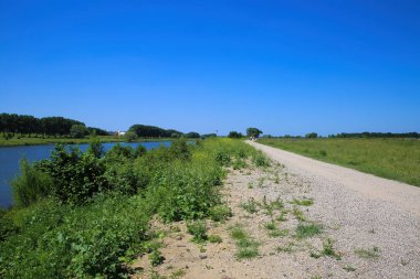 Hollanda, Venlo yakınlarındaki Maas nehri boyunca yaz aylarında tipik bir kırsal alandaki toprak bisiklet pistine bakın.