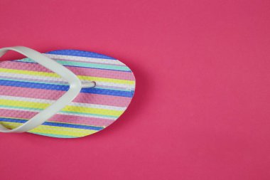 İzole edilmiş renkli çizgili çift parmak arası terliklerin üzerine pembe arka planda fotokopi alanı ile üst görünüm