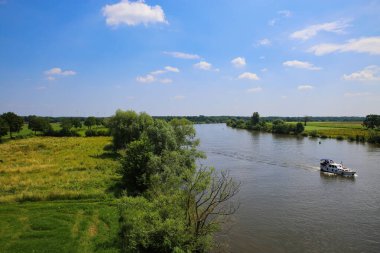 Hollanda, Limburg yakınlarındaki mavi gökyüzüne karşı yaz aylarında nehir maaları ve yeşil tarım arazileri ile tipik Hollanda kırsal manzarası üzerine panoramik manzara