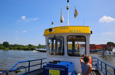 Blitterswijck, Hollanda - 1 Temmuz. 2021: Küçük yolcu ve bisiklet feribotunun (voet- en fietsveer) nehir maas, konteyner gemi arkaplan yaz (kabin odaklı) sürücü kabin görüntüsü)