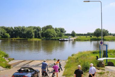 Broekhuizen, Hollanda - 1 Temmuz. 2021: Yolcu, araba ve bisiklet feribotunu nehir üzerinden Arcen 'e bekleyen insanların görüntüsü