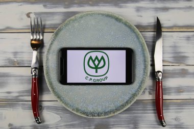 Viersen, Almanya - 9 Mayıs. 2021: Tabak ve ahşap masadaki cep telefonunun kapatılması, Thai Cp grubunun logo harfli çatal bıçak takımı (merkeze odaklan)