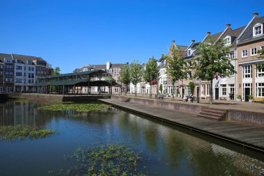 Helmond, Hollanda - 10 Temmuz. 2021: Mavi gökyüzü olan geleneksel Hollandalı evleri su kanalından izleyin