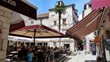 Trogir, Hırvatistan - 9 Mayıs. 2017: Ortaçağ şehrinin meydanında yaz aylarında şemsiyeler altında açık havada restoranda oturan insanların görüntüsü
