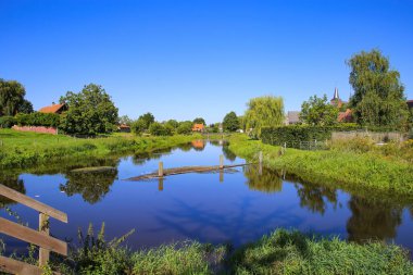 Hollanda 'da sakin sakin sakin yürüyüş parkurlarına, yemyeşil çayır ve ağaçlara, derin mavi bulutsuz yaz gökyüzüne, küçük köy arka planına Neer (Limburg), Hollanda