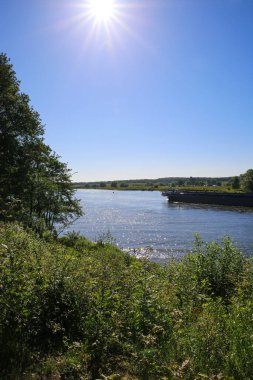 Hollanda 'nın Roermond ve Venlo kentleri arasında mavi yaz gökyüzü ile Maas nehrinin yeşil kırsal manzarasına bakın.