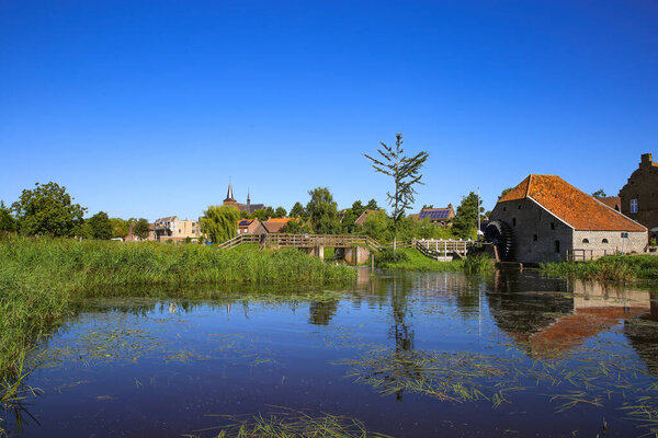 View over reflecting river pond on old water mill restaurant against deep blue cloudless summer sky - Neer (Limburg), Netherlands