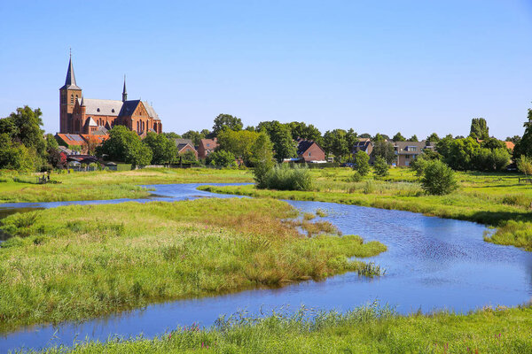 View over green wetland water on cityscape of durch town with tower of medieval church against blue summer sky - Neer (Limburg), Netherlands