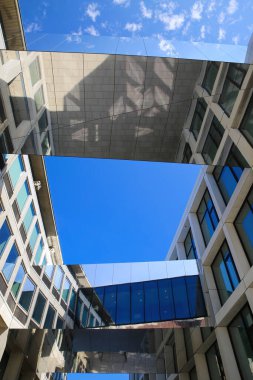 Arnhem (il evi), Hollanda - 9 Temmuz. 2021: Açık mavi gökyüzüne karşı iki ofis binası arasındaki gökyüzü köprülerini yansıtan metal camlı ev kanyonunun alçak açısı