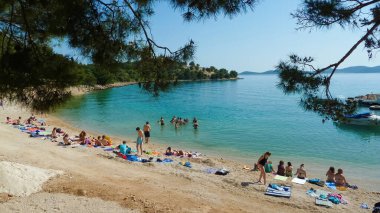 Drage, Hırvatistan - 9 Mayıs. 2015: Çam ağacı dallarının ötesine, Adriyatik Denizi 'nde kumsalda insanlarla birlikte, adanın arka planına bak (plajın merkezine odaklan)