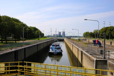 Roermond (Heel), Hollanda - 9 Temmuz. 2021: Kargo gemisiyle Maas nehrindeki kapak kapağında, RWE elektrik santralinin arka planında bulanık kuleler