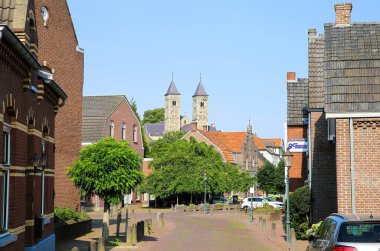 Sint Odilienberg, Hollanda - 9. Temmuz 2021: 11. yüzyıldan kalma Roma bazilikasındaki evlerin ötesindeki caddenin mavi yaz gökyüzüne karşı görüntüsü